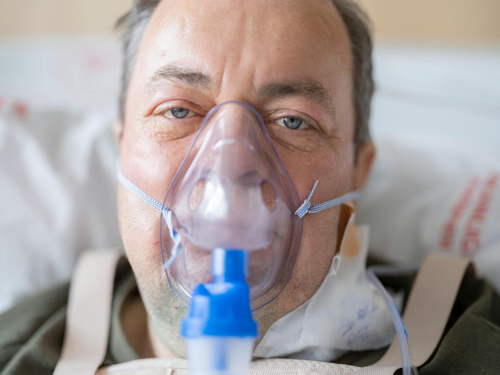Mężczyzna w szpitalnym łóżku oddycha przez maskę tlenową