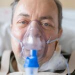 Mężczyzna w szpitalnym łóżku z maską tlenową na twarzy