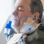 Starszy pacjent w szpitalu oddychający przez maskę tlenową