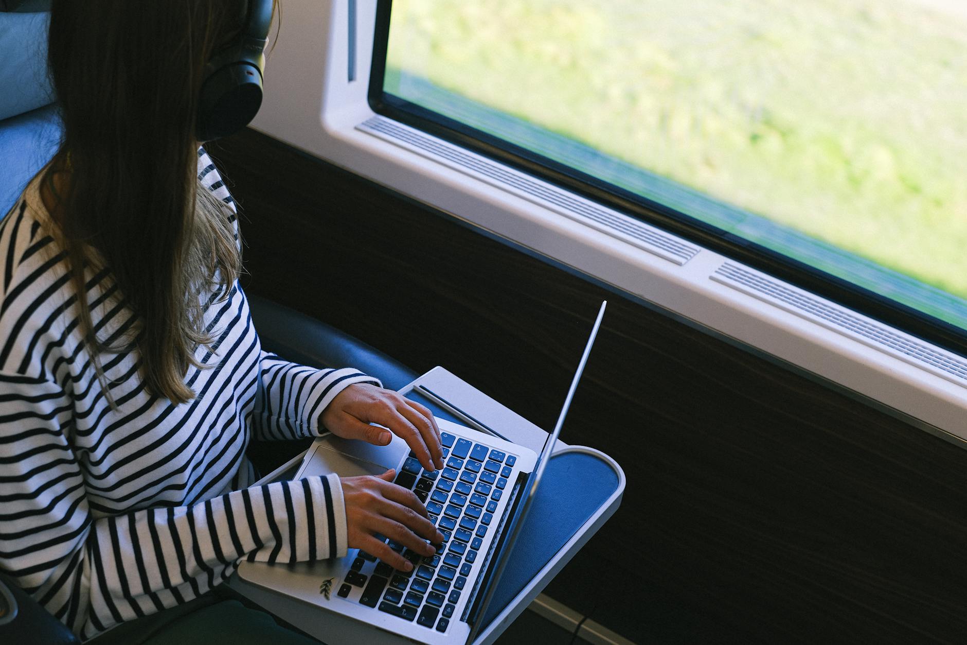 Osoba w słuchawkach pracuje na laptopie podczas podróży pociągiem