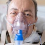 Mężczyzna w szpitalnym łóżku z maską tlenową na twarzy