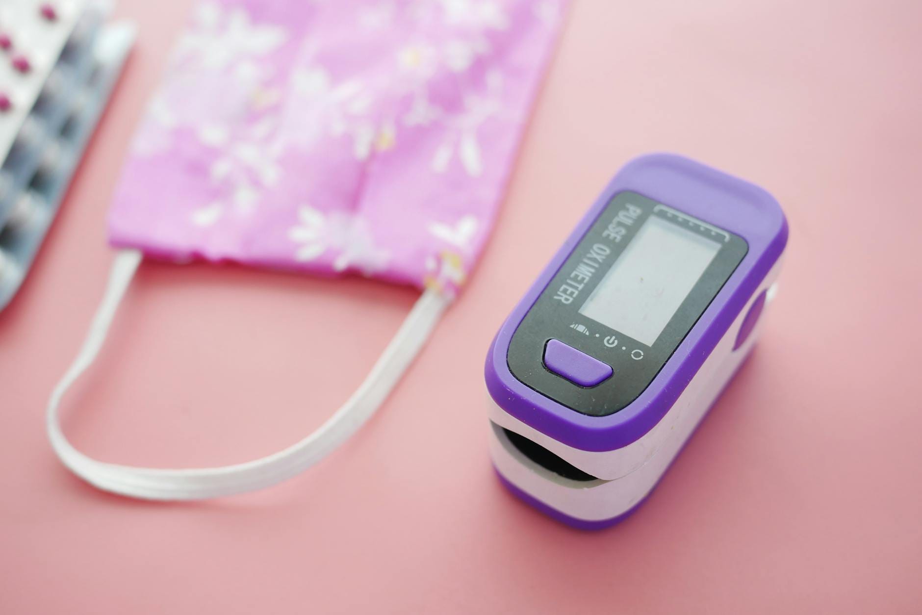 Pulsoksymetr i maseczka we wzory kwiatowe na różowym tle