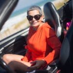 Starsza kobieta w pomarańczowej sukience siedzi w kabriolecie nad morzem
