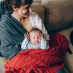 Mama trzyma śpiącego noworodka otulonego miękkim kocykiem
