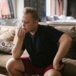 Mężczyzna w pomieszczeniu pali skręta, siedząc w swobodnej pozie