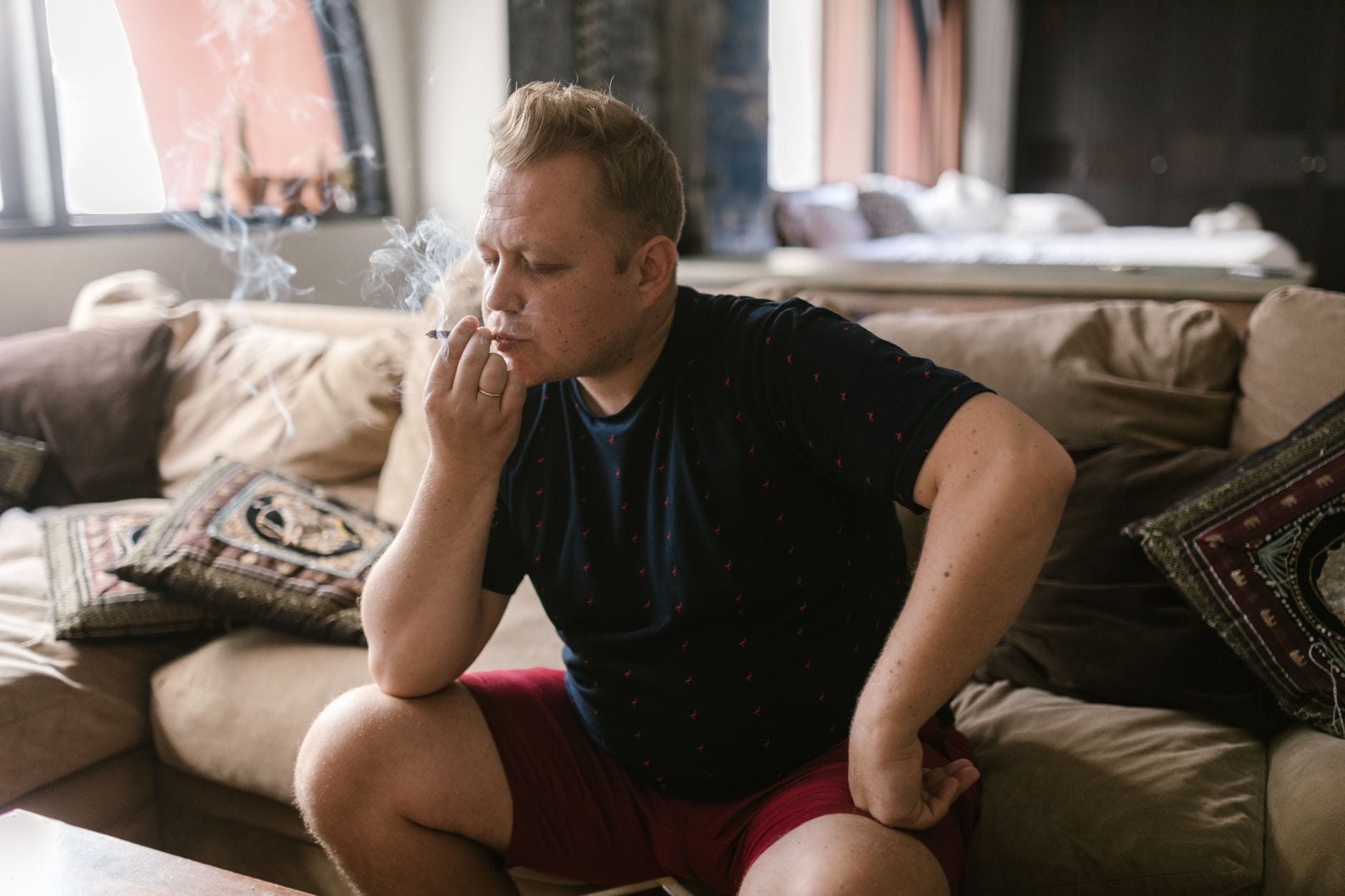Mężczyzna w pomieszczeniu pali skręta, siedząc w swobodnej pozie