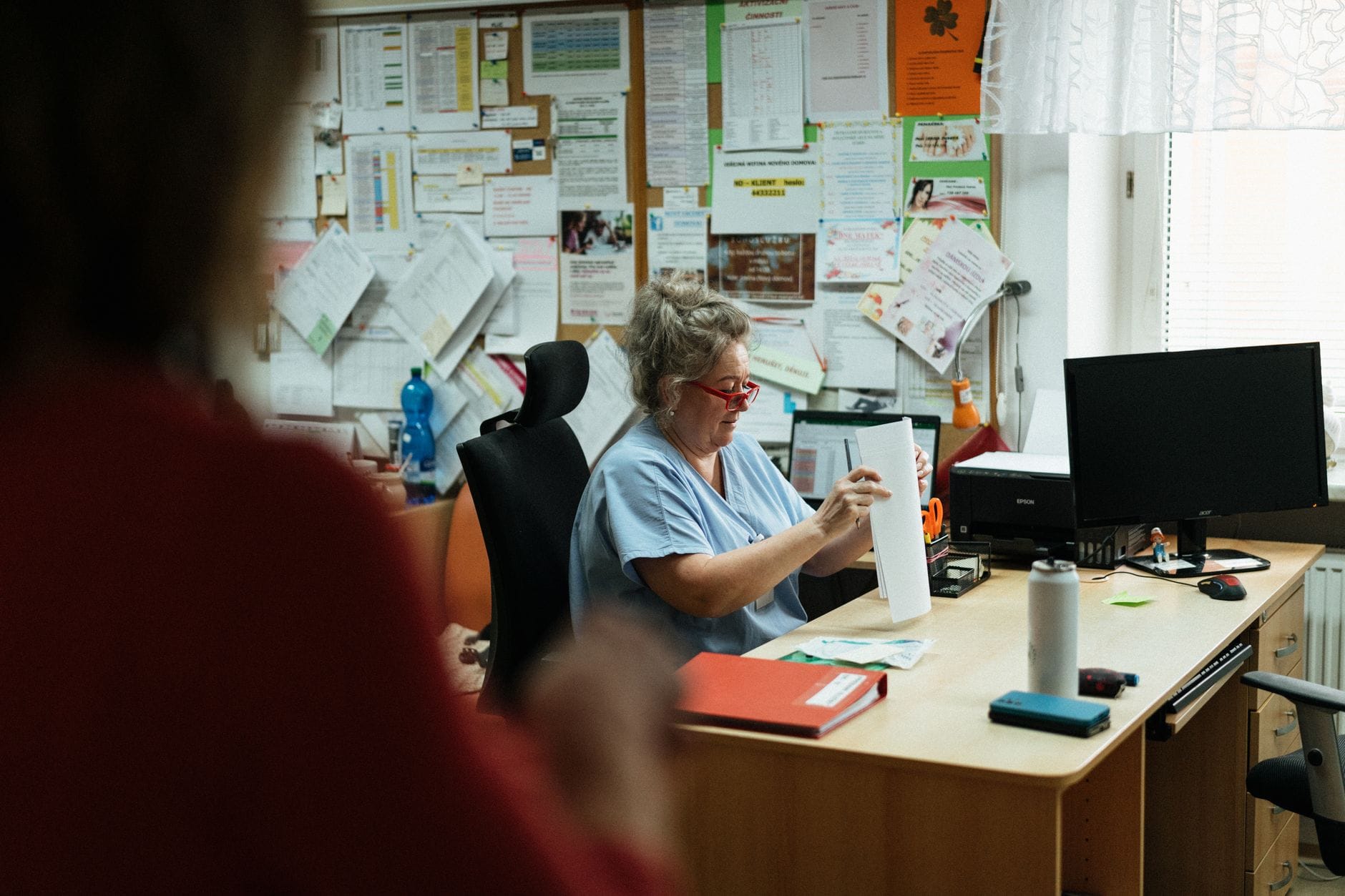 Opiekun medyczny w niebieskim uniformie porządkuje dokumenty przy biurku
