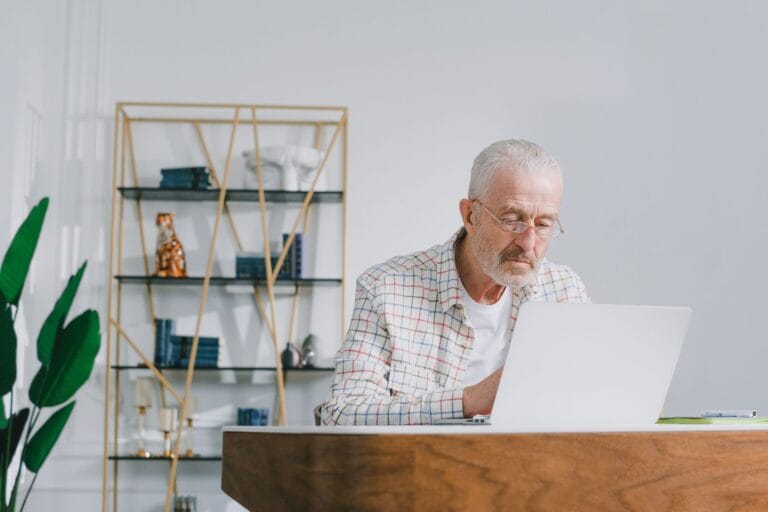 Starszy mężczyzna korzystający z laptopa w jasnym pokoju w domu